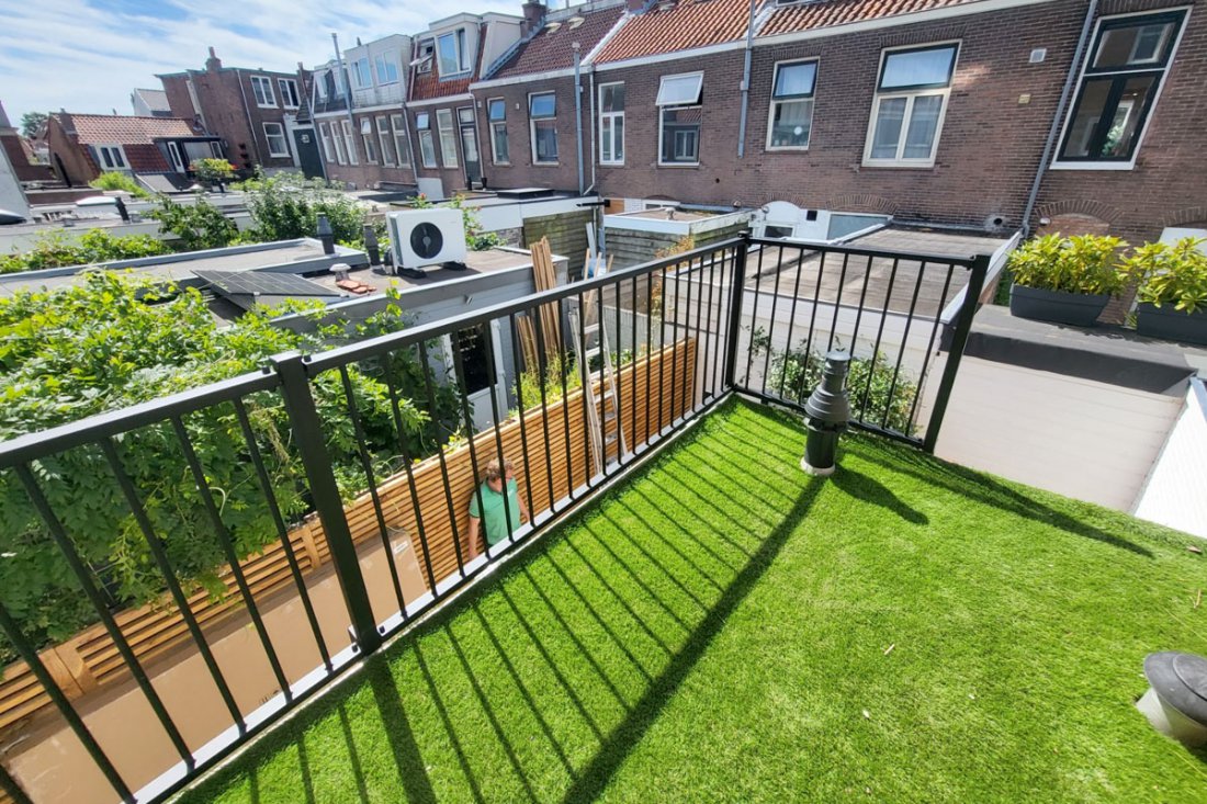 Goed onderhouden zwart balkonhekwerk langs een terras met kunstgras