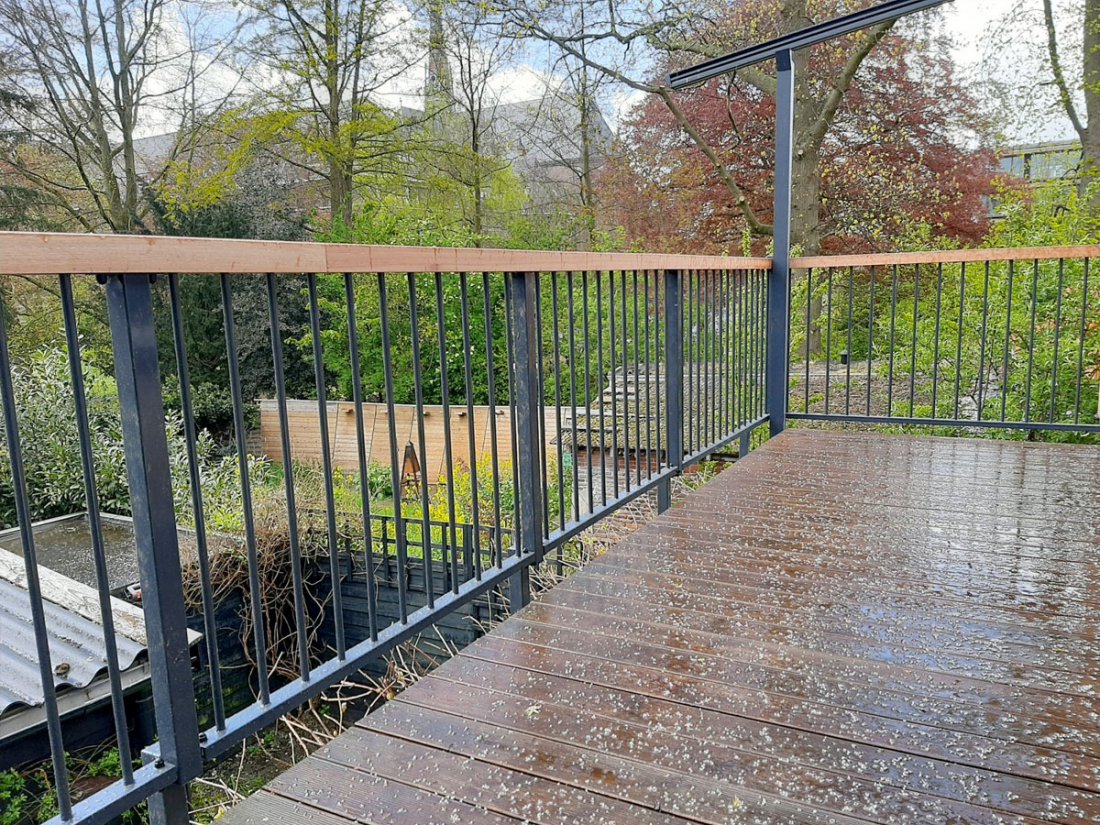 Hekwerk met een houten handregel langs een dakterras in het groen