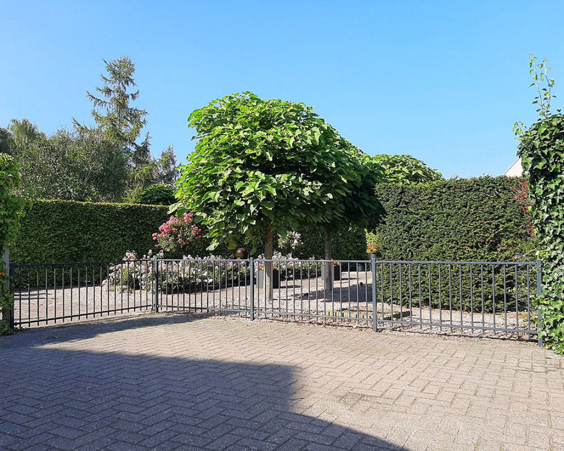 Tuinhekwerk als erfafscheiding voor een oprit met heg en bomen