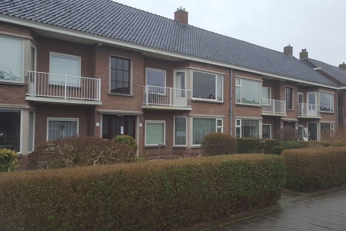 Hekwerk langs een lang gebouw met een groenstrook ervoor