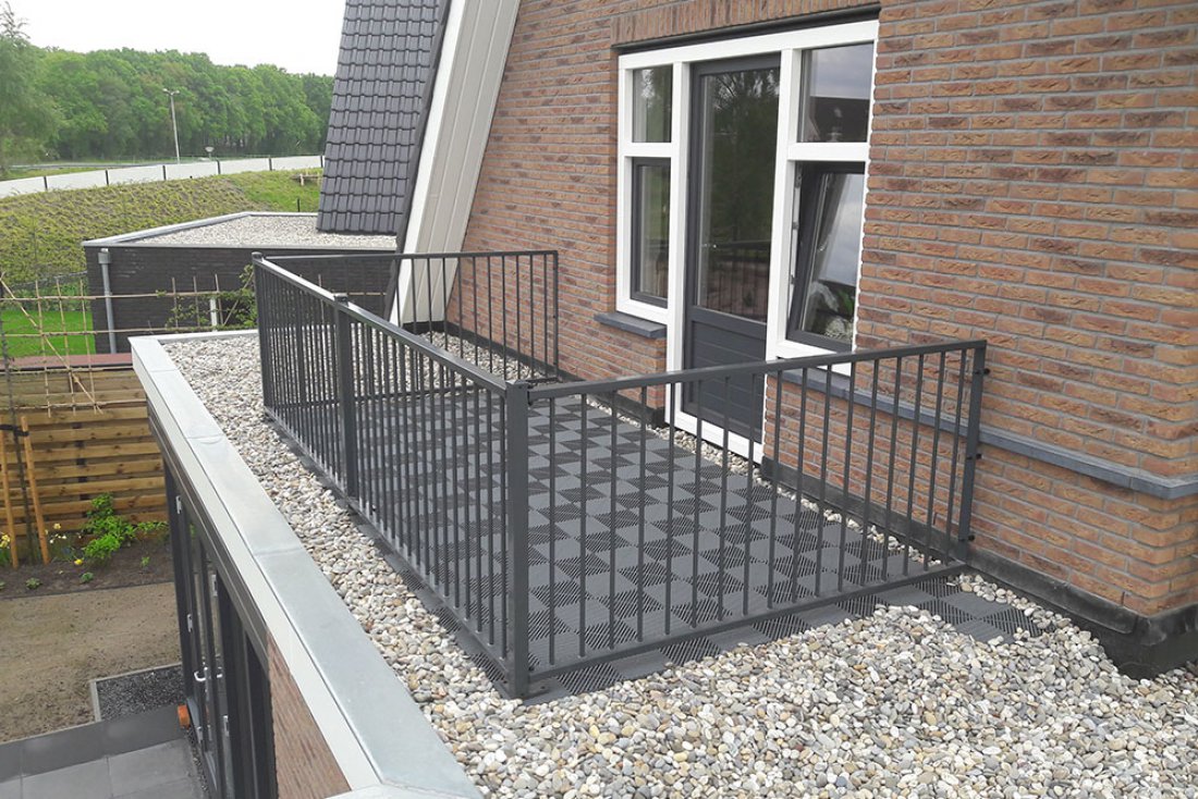 Hekwerk langs een terrein met grind naast een gebouw