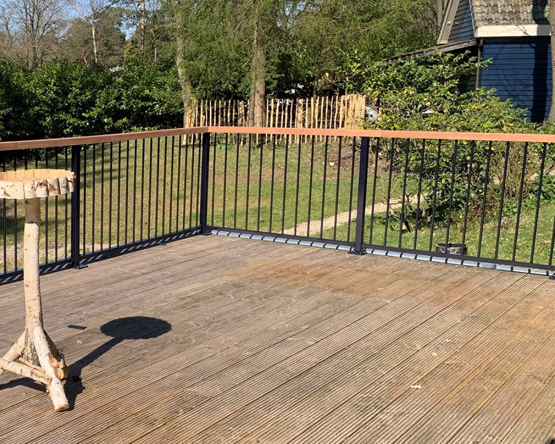 Stalen hekwerk langs een houten vlonder met beplanting
