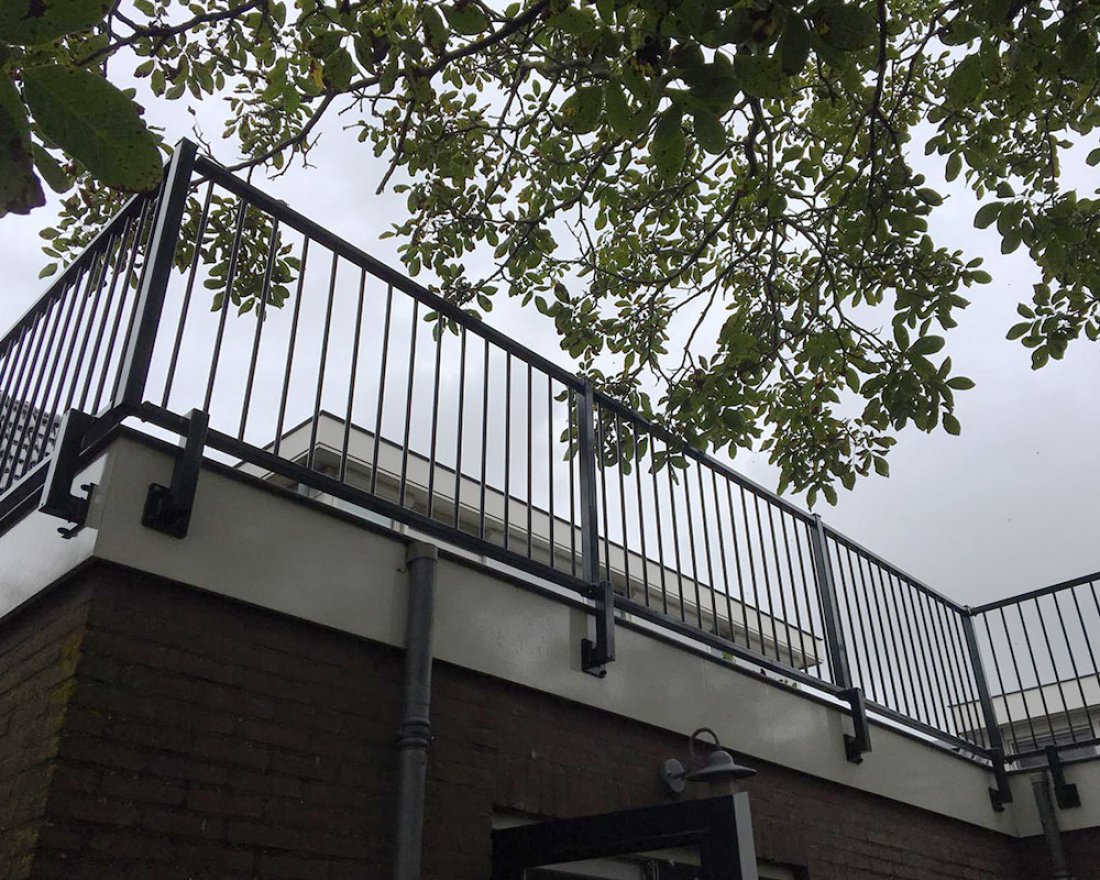 Stalen hekwerk langs een terras onder de bomen